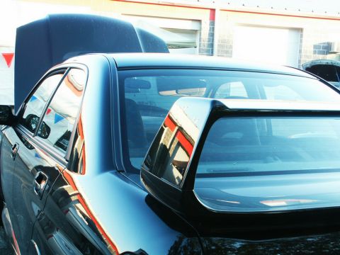 2001 Mercury Grand Marquis - A black sedan's rear spoiler and open hood are visible, reflecting a building with red and white stripes.