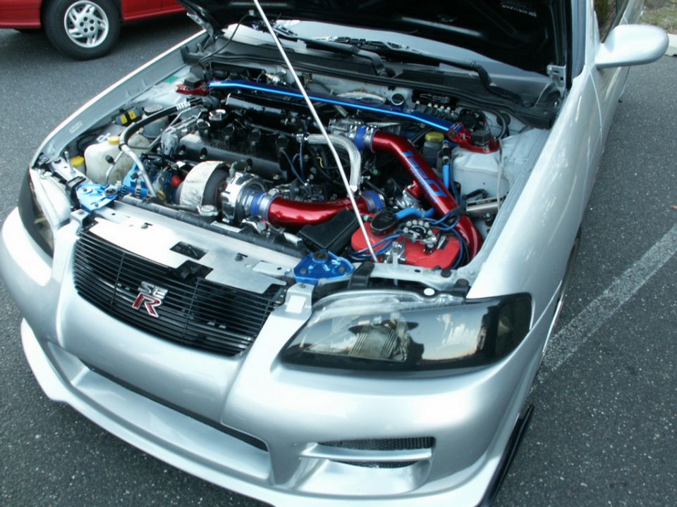 Silver car engine bay with turbocharger and red piping. Supermotors.net logo visible