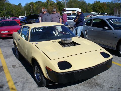 1991 Ford Probe - A yellow sports car with a modified hood exposing the engine sits parked at an outdoor event.