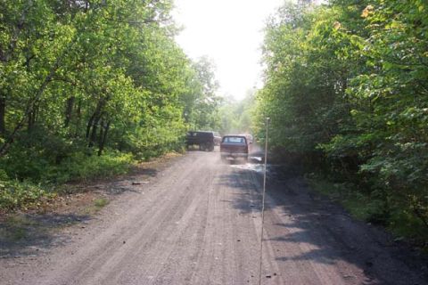 Two SUVs driving on a dusty dirt road surrounded by trees