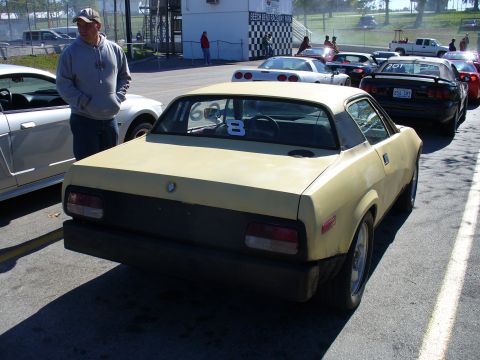 1991 Ford Probe - Yellow coupe with racing number 8 parked at a track event, other vehicles present.