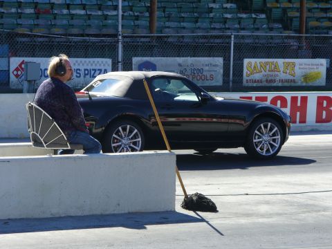 1991 Ford Probe - A black convertible sits on the track at a drag racing event, with a spectator in headphones watching.