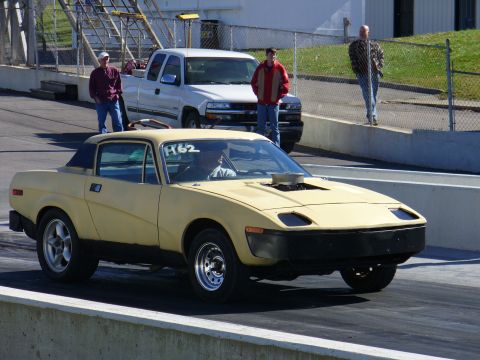 1991 Ford Probe - A yellow sports car with a hood scoop and racing number F62 is on a drag strip, with a white pickup truck in the background.