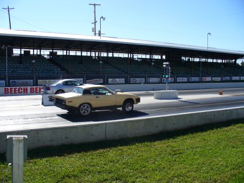 1991 Ford Probe - Two cars race down a drag strip under a clear blue sky, with grandstands visible.