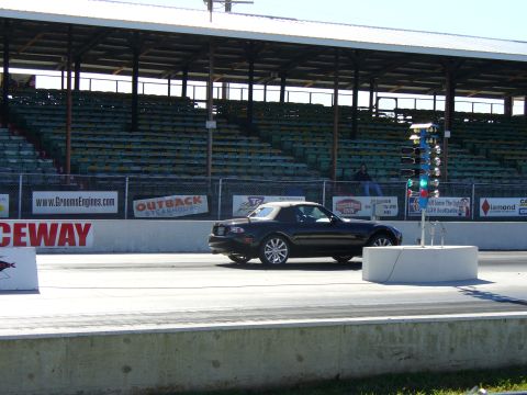 1991 Ford Probe - A black convertible drives down the drag strip past the starting lights.
