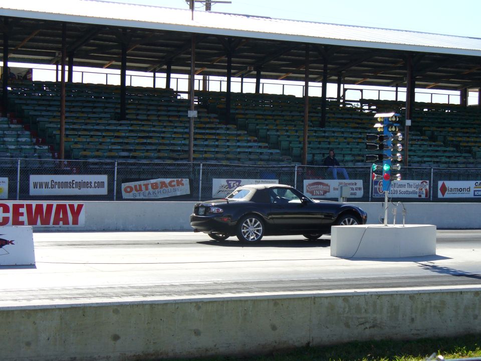 Black convertible sports car on a drag strip with bleachers in the background