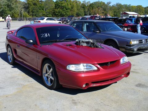 1991 Ford Probe - A red coupe with a custom hood scoop and exposed engine is parked outdoors next to other vehicles.