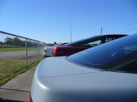 1991 Ford Probe - Multiple cars are parked in a row next to a chain-link fence on a sunny day.