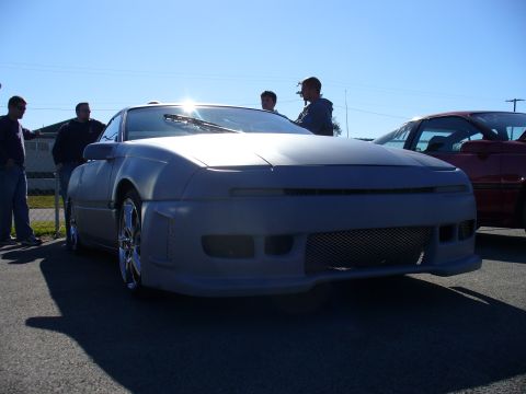 1991 Ford Probe - A gray car with an aftermarket body kit is parked outdoors, with other people and vehicles in the background.