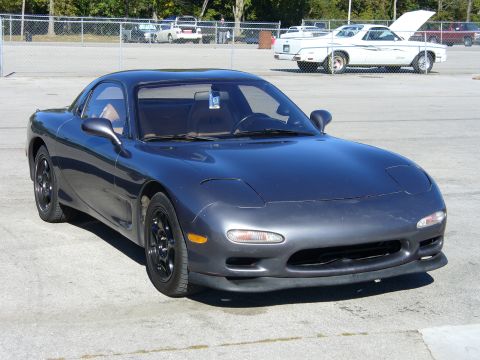 1991 Ford Probe - A dark gray Mazda RX-7 is parked in an outdoor lot, with a white El Camino visible behind it.