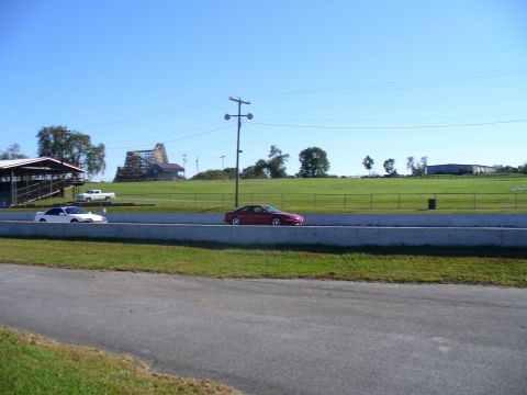 1991 Ford Probe - Two cars and a truck are visible on a sunny day at a racetrack, with a distinctive building in the background.