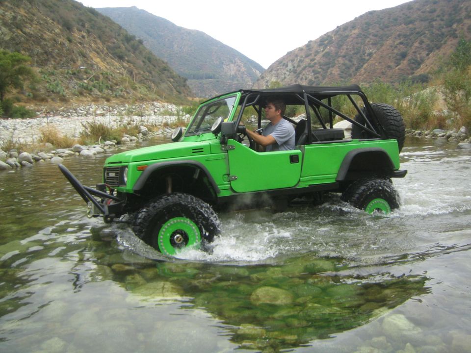 Green 1987 Suzuki Samurai driving through river