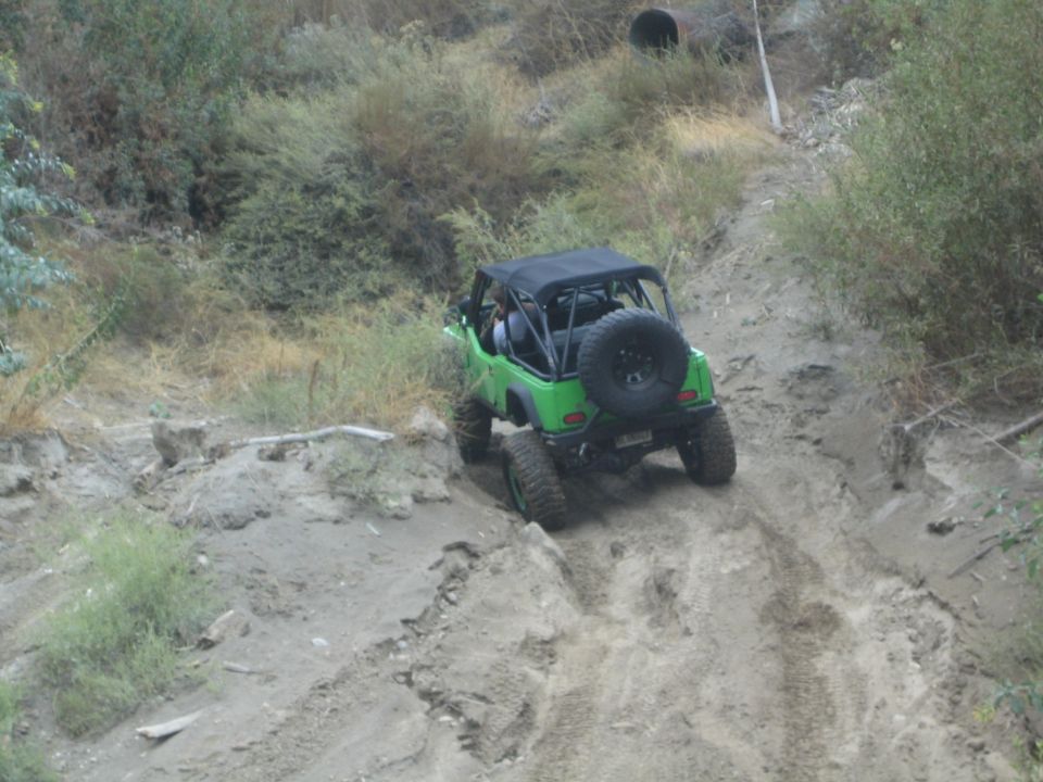 Green off-road vehicle with spare tire on rear, driving on a dirt trail