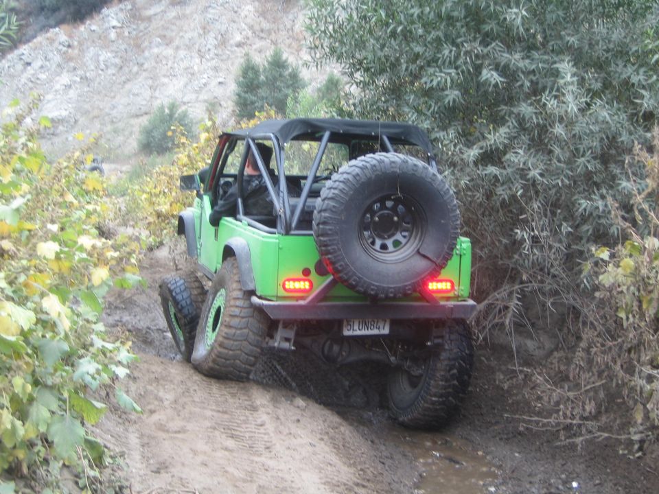 Green off-road vehicle with a spare tire on the back, driving on a muddy trail