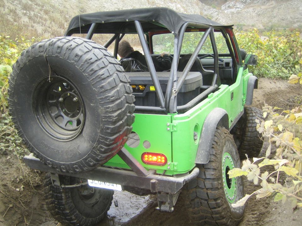 Green off-road vehicle with a spare tire mounted on the back, driving on a dirt trail