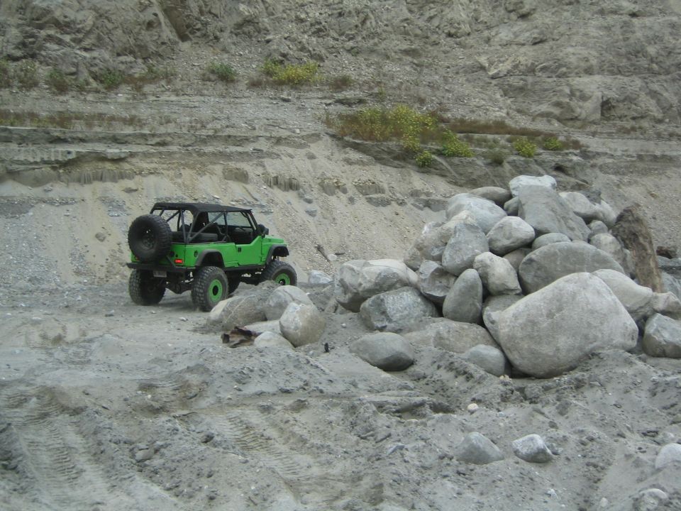 Green off-road vehicle with spare tire on back parked on dirt road near pile of rocks