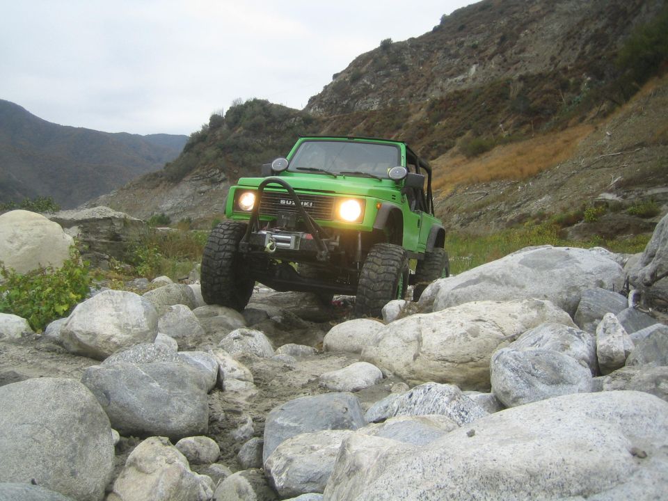1987 Suzuki Samurai driving over large rocks in a dry riverbed