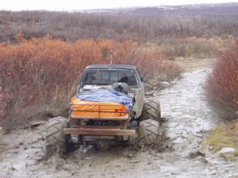 2000 Ford E350 - A heavily modified pickup truck is stuck in thick mud on an off-road trail.
