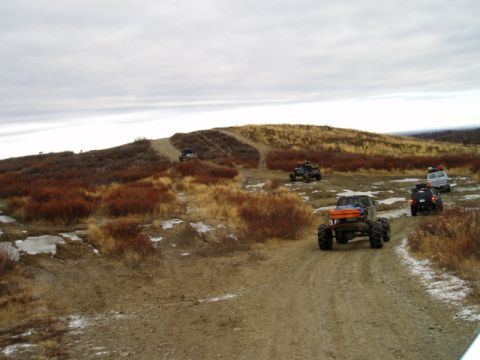 2000 Ford E350 - Multiple off-road vehicles traverse a dirt trail in a barren, hilly terrain with scattered snow patches of snow.