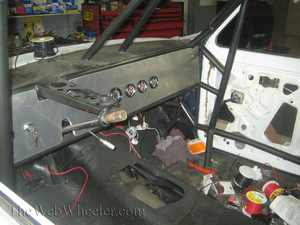 Interior of a vehicle with a roll cage, custom dashboard with gauges, and exposed wiring