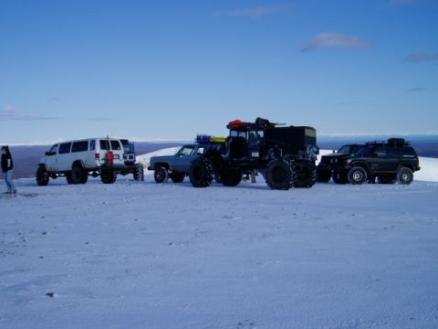 2000 Ford E350 - Several modified vehicles are parked in a snowy, open area under a clear blue sky.