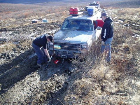 2000 Ford E350 - Men use a winch to free a pickup truck stuck in a muddy track in a desolate area.
