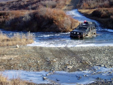 2000 Ford E350 - A vehicle navigates a cold river, with ice forming along the shore and a dirt track leading away.