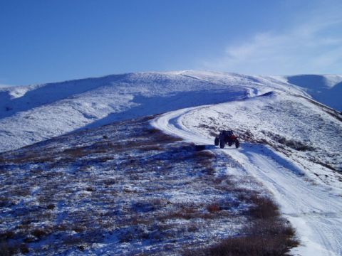2000 Ford E350 - A red off-road vehicle navigates a snow-covered dirt road winding through a barren, snow-dusted landscape under a clear blue sky.