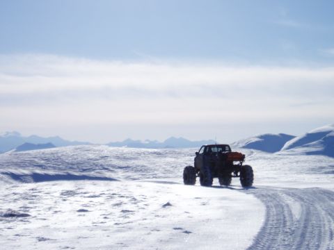 2000 Ford E350 - A heavily modified truck navigates a snowy terrain, its off-road capabilities against a backdrop of distant mountains.