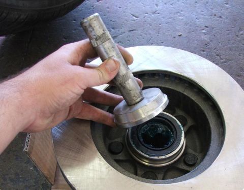 1985 Ford Crown Victoria LTD - A hand uses a tool to grease a wheel bearing installed in a brake rotor, with a Supermotors.net watermark visible.