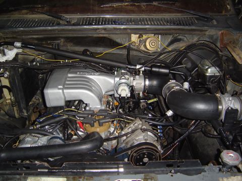 1986 Ford Bronco - Engine bay a silver intake manifold and various hoses and components.