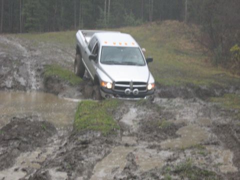 1995 Ford Bronco - A silver pickup truck struggles through a muddy terrain with water splashing around it.