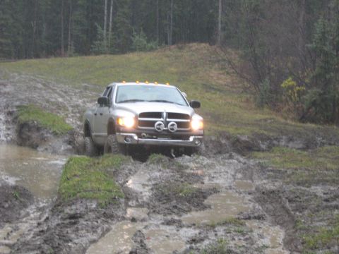 1995 Ford Bronco - Pickup truck driving through a muddy off-road course.