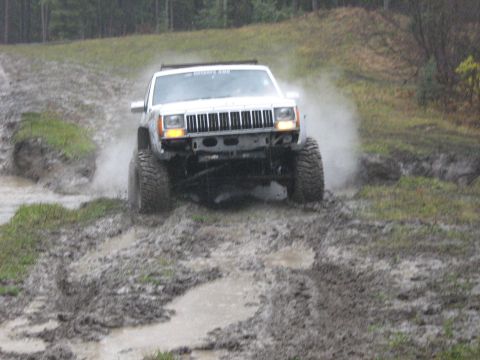 1995 Ford Bronco - This Jeep Cherokee XJ is navigating a challenging muddy terrain, with water splashing around its tires.