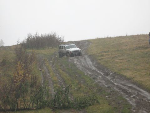 1995 Ford Bronco - A white SUV navigates a challenging muddy incline on a cloudy day.