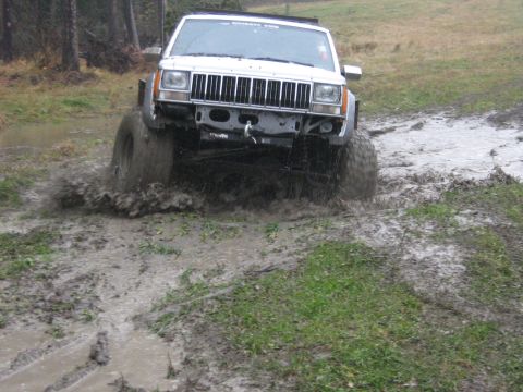 1995 Ford Bronco - This modified Jeep Cherokee XJ navigates a challenging muddy terrain, kicking up water and dirt.
