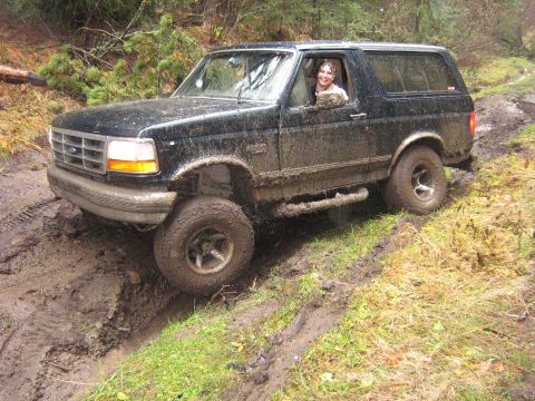 1995 Ford Bronco - A black 1995 Ford Bronco tackles a challenging muddy path, with a driver visible behind the wheel.