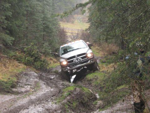 1995 Ford Bronco - A Dodge Ram pickup truck is shown off-roading on a wet, muddy path in a forest.