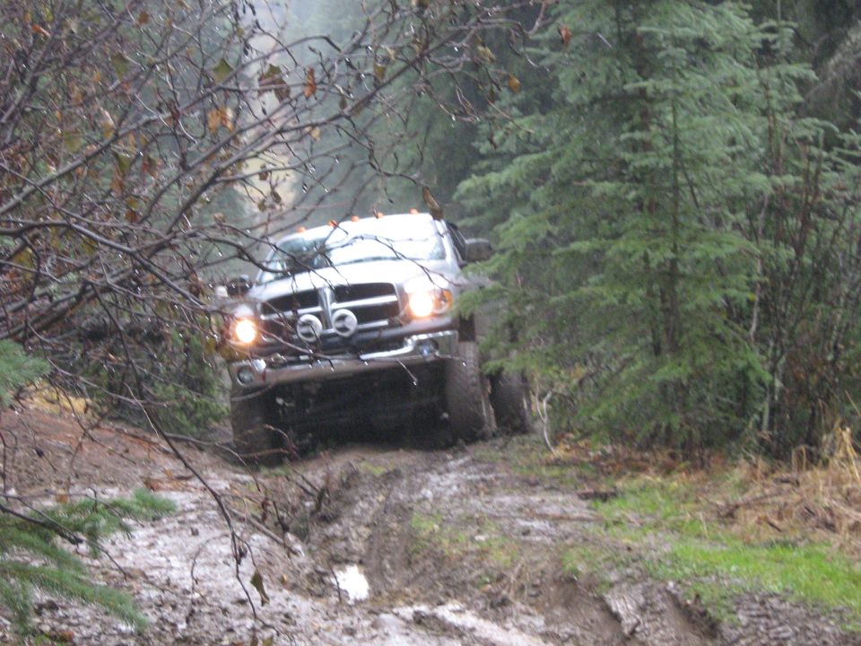 Lifted Dodge Ram pickup with lights on descending a rutted muddy forest trail
