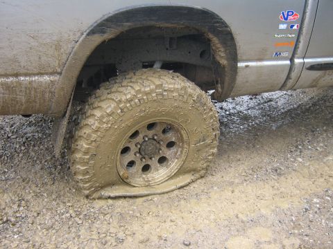 1995 Ford Bronco - A flat tire on a mud-splattered truck is visible on a rough, wet surface.