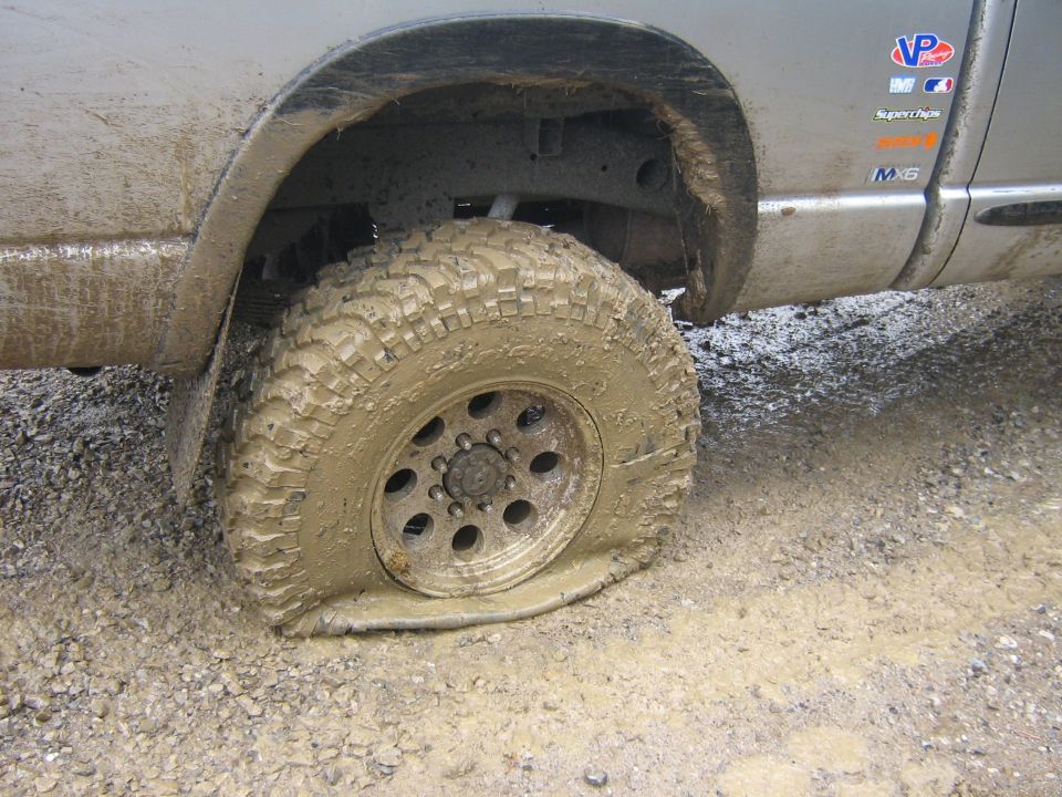 Mud-covered truck side with flat tire on gravel and mud