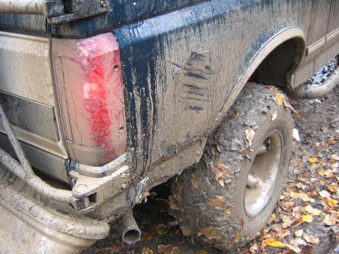 1995 Ford Bronco - Mud-caked rear of a 1995 Ford Bronco, showing the tail light and tire, with fallen leaves on the ground.