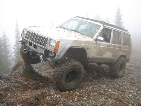 1995 Ford Bronco - This modified Jeep Cherokee XJ is shown navigating a challenging, rocky terrain on a foggy day.