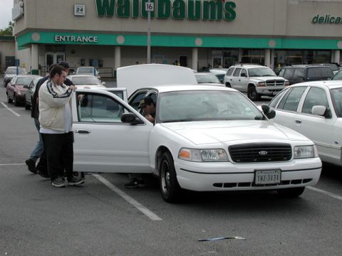 1998 Ford Crown Victoria - A white 1998 Ford Crown Victoria is parked with its doors open, showing people interacting with the vehicle.