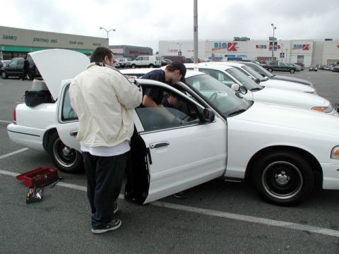 1998 Ford Crown Victoria - Two men are working on a white 1998 Ford Crown Victoria in a parking lot.