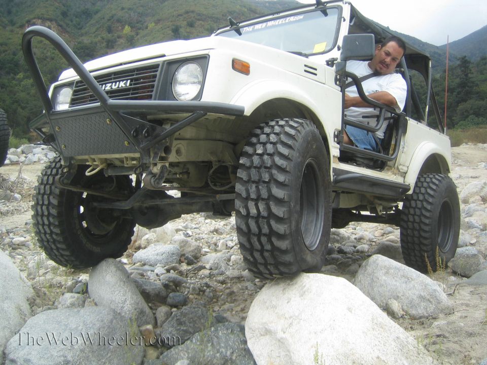 White 1987 Suzuki Samurai with a custom bumper driving over rocks