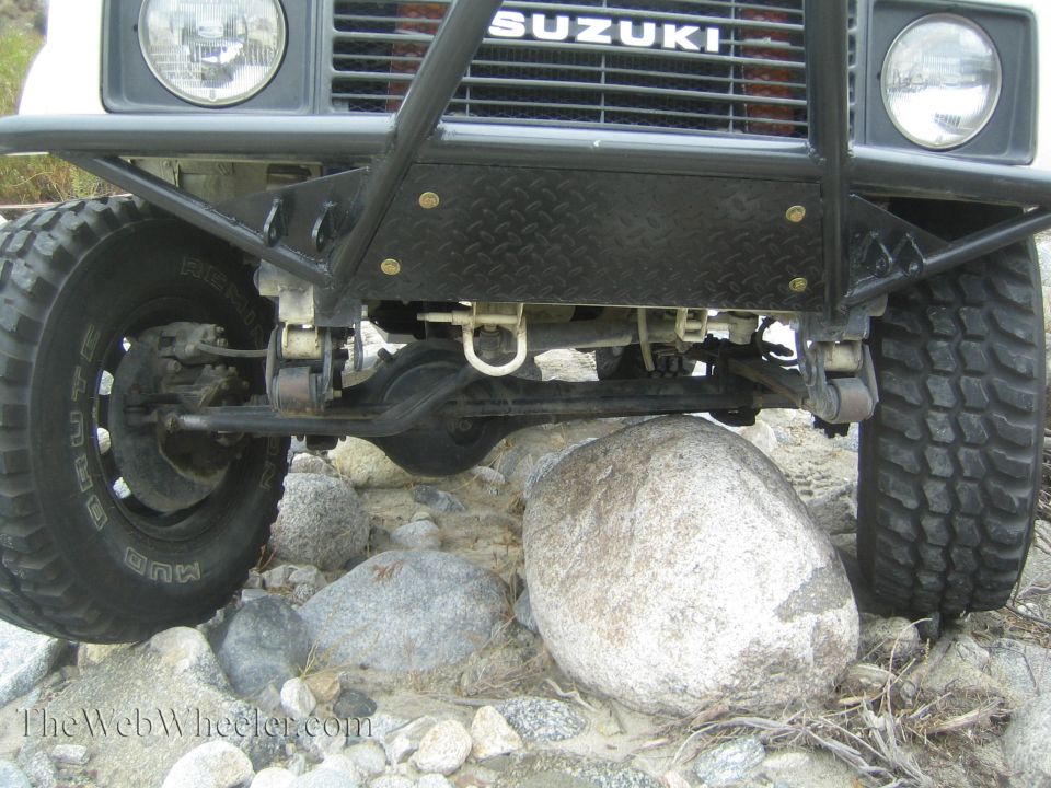 Front of a 1987 Suzuki Samurai with a custom bumper, tires on rocks