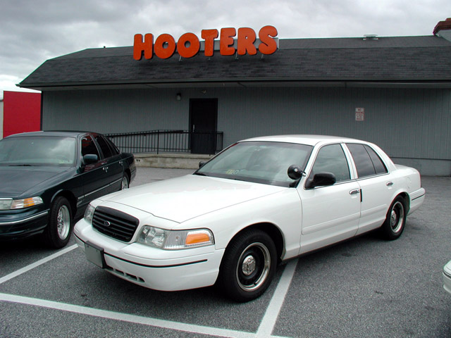 White Ford Crown Victoria sedan parked outside a Hooters restaurant