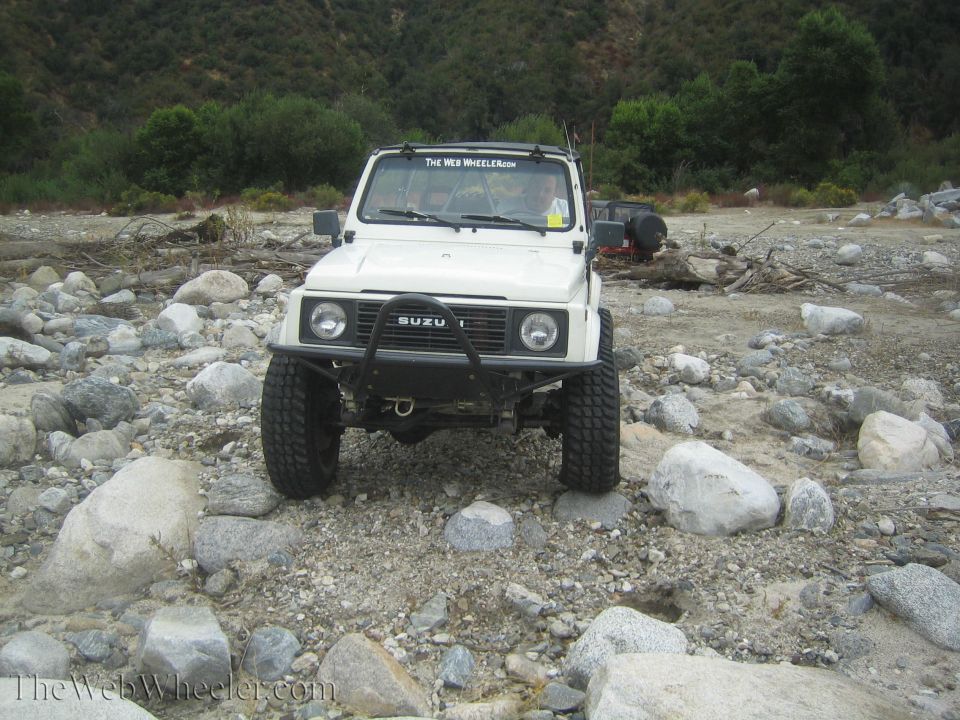 White SUV with off-road tires on rocky terrain. Has 'ISUZU' on the grille