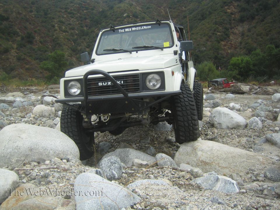 White Suzuki Samurai with off-road tires on rocks. "The Web Wheeler" sticker on windshield